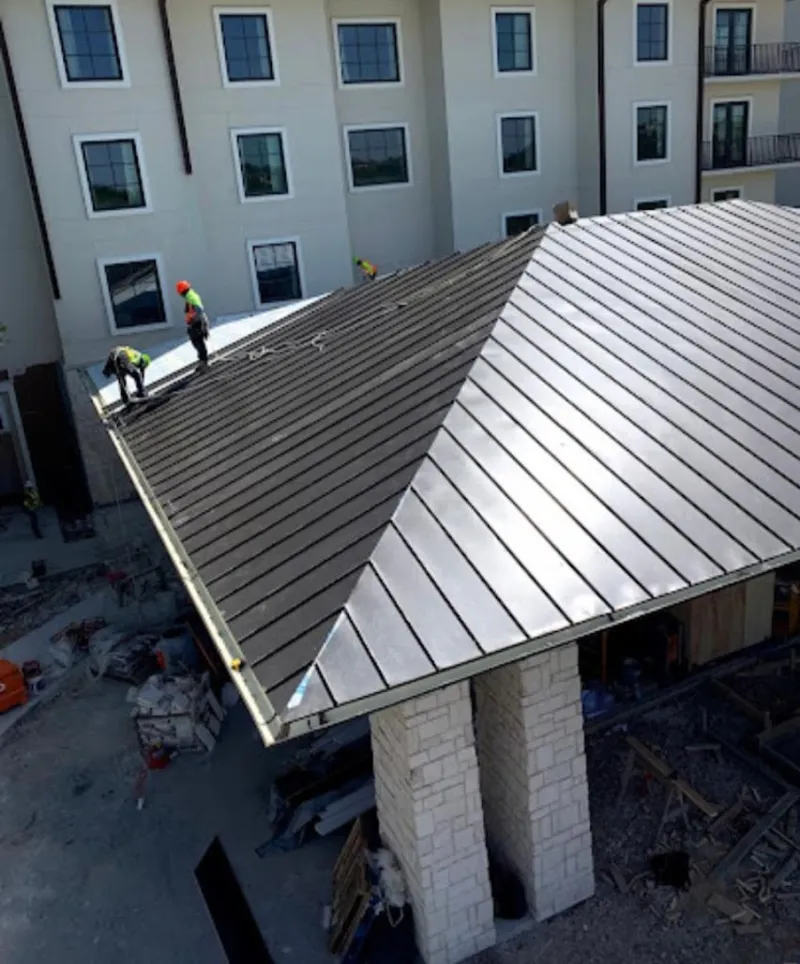 Crew installing standing seam metal roof panels on a commercial project in Manor
